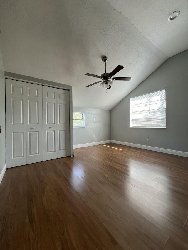 unfurnished bedroom featuring vaulted ceiling, a textured ceiling, baseboards, and wood finished floors