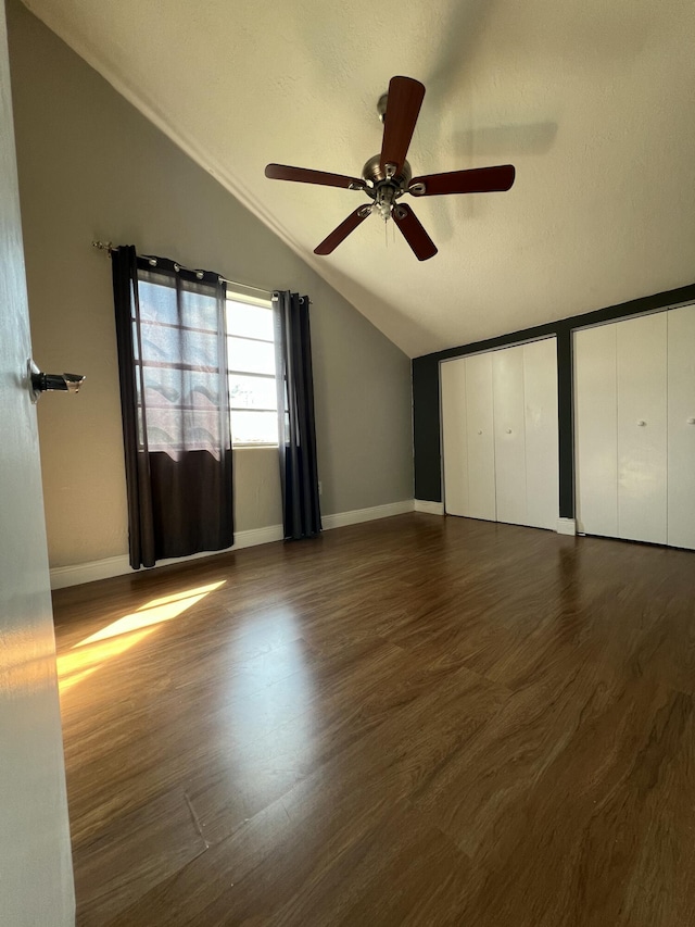 unfurnished bedroom featuring lofted ceiling, dark wood-type flooring, baseboards, and multiple closets