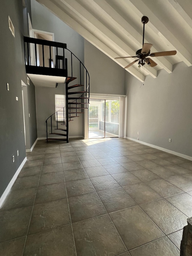 unfurnished living room with a ceiling fan, high vaulted ceiling, beamed ceiling, baseboards, and stairs