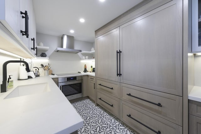 kitchen with oven, a sink, light countertops, wall chimney range hood, and open shelves