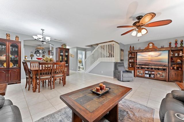 living area featuring stairs, light tile patterned floors, ceiling fan with notable chandelier, and baseboards