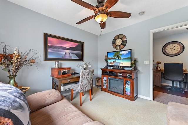 living area with a ceiling fan, carpet, a glass covered fireplace, and baseboards