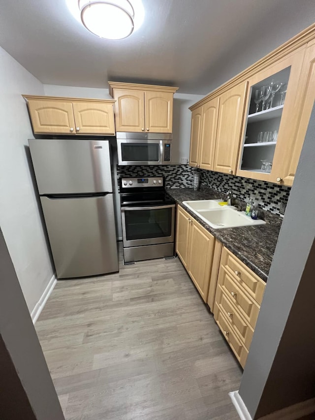 kitchen featuring a sink, appliances with stainless steel finishes, light brown cabinetry, tasteful backsplash, and glass insert cabinets