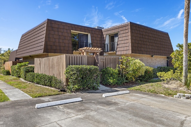 exterior space with uncovered parking, fence, mansard roof, and brick siding