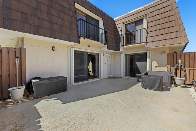 rear view of property with a patio area, stucco siding, a balcony, and mansard roof