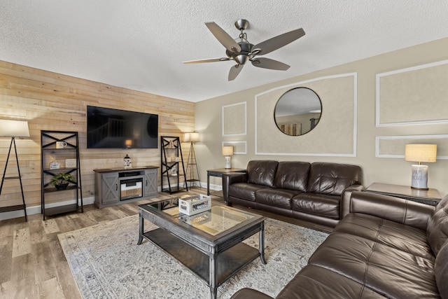 living room with wood walls, a textured ceiling, a ceiling fan, and wood finished floors