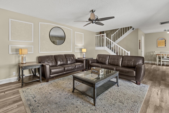 living area with a textured ceiling, stairs, visible vents, and wood finished floors