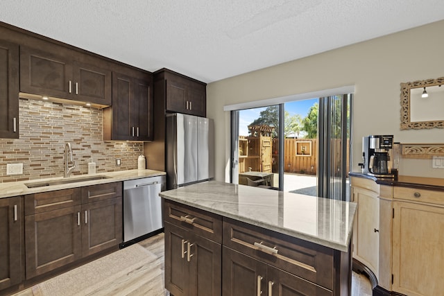 kitchen with dark brown cabinetry, light stone countertops, stainless steel appliances, a sink, and decorative backsplash