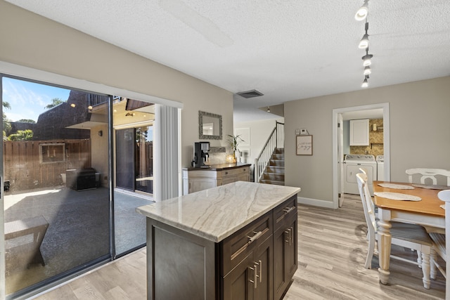 kitchen with light stone countertops, light wood-style flooring, a textured ceiling, and washing machine and clothes dryer