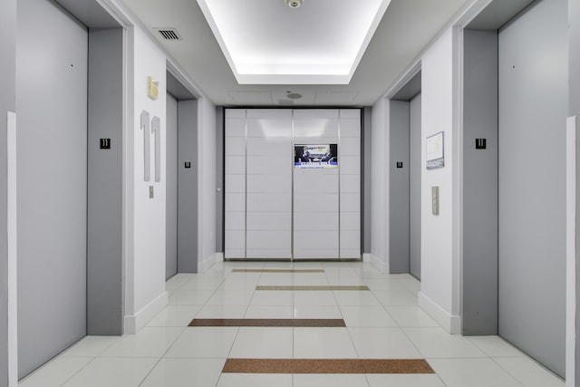 corridor featuring light tile patterned floors, baseboards, and elevator