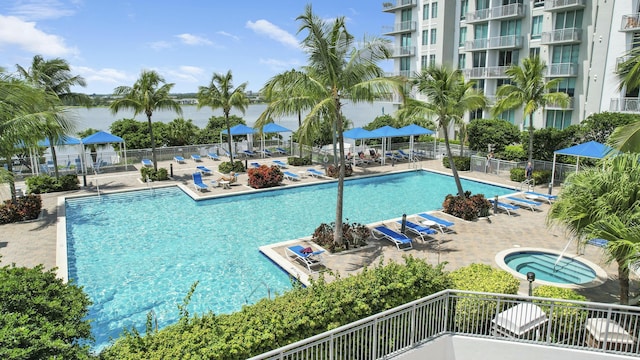 community pool with a water view, fence, a hot tub, and a patio