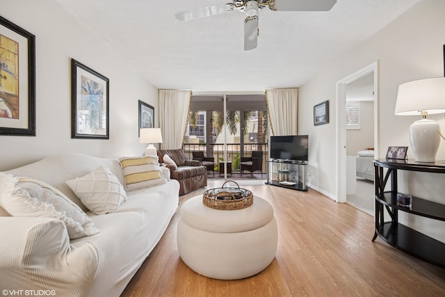 living room with a ceiling fan, a textured ceiling, baseboards, and wood finished floors