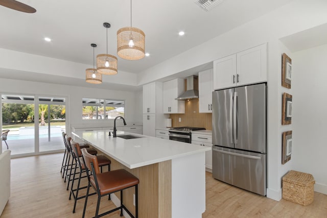 kitchen with light wood finished floors, visible vents, wall chimney exhaust hood, appliances with stainless steel finishes, and a sink