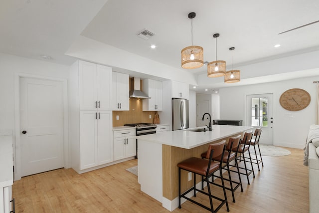 kitchen with wall chimney exhaust hood, visible vents, appliances with stainless steel finishes, and light wood-style flooring