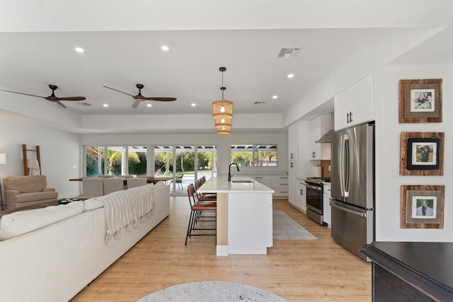 kitchen featuring visible vents, appliances with stainless steel finishes, open floor plan, white cabinets, and a sink