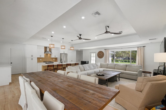 living area featuring ceiling fan, recessed lighting, visible vents, light wood-type flooring, and a tray ceiling