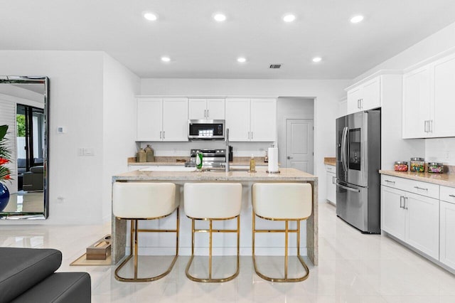 kitchen with an island with sink, a breakfast bar, stainless steel appliances, white cabinetry, and recessed lighting