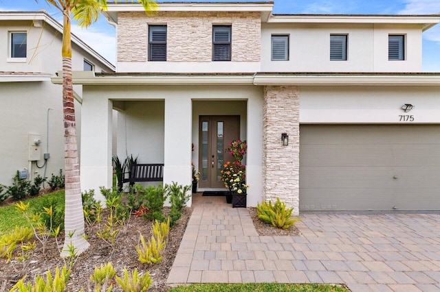 view of front of property featuring a garage, stone siding, decorative driveway, and stucco siding