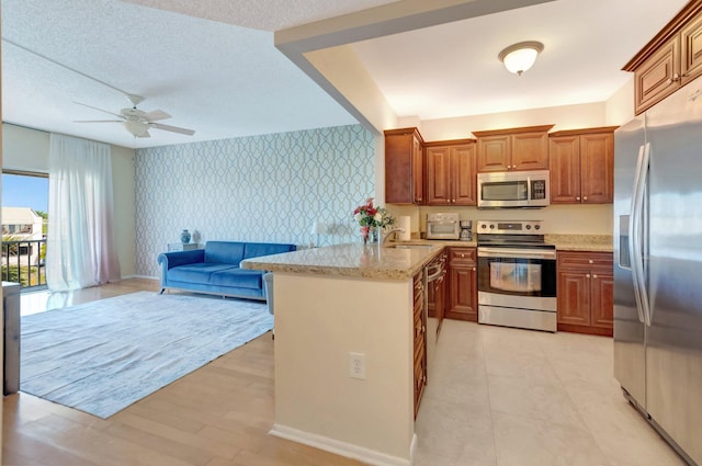 kitchen with a textured ceiling, a peninsula, wallpapered walls, and stainless steel appliances