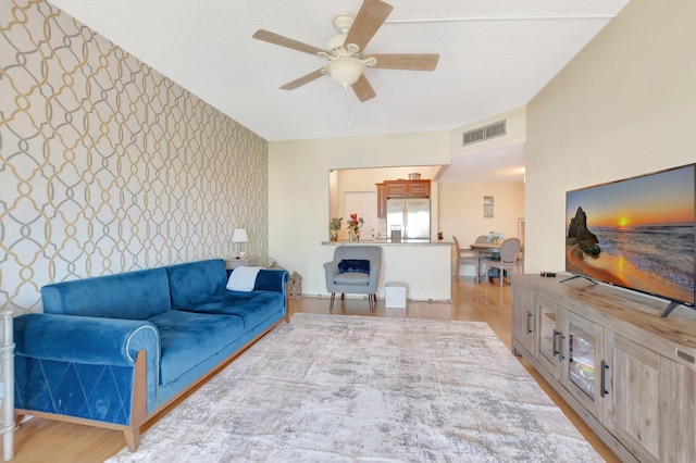 living room with visible vents, light wood-style floors, wallpapered walls, ceiling fan, and an accent wall