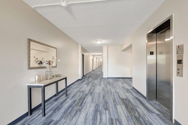 corridor with elevator, a textured ceiling, baseboards, and wood finished floors