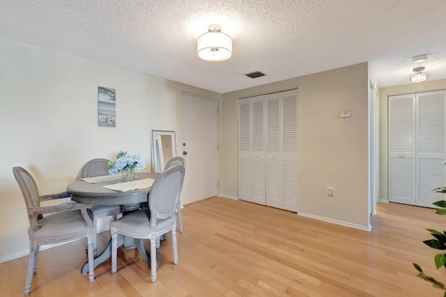 dining area with light wood-type flooring, visible vents, and baseboards