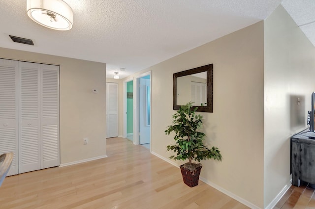 hallway with visible vents, light wood-style flooring, a textured ceiling, and baseboards