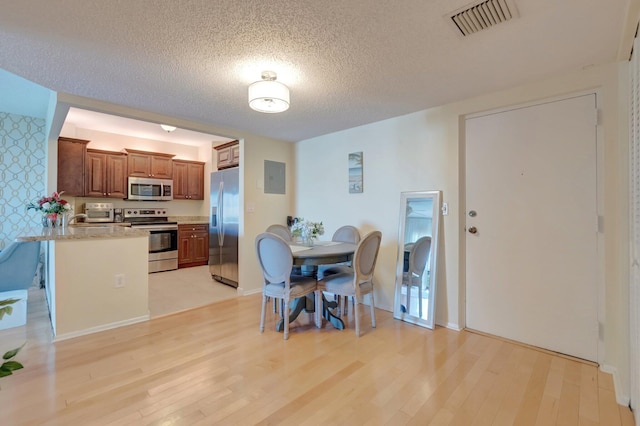 dining space featuring electric panel, light wood-style floors, visible vents, and a textured ceiling