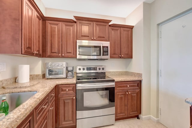 kitchen featuring baseboards, stainless steel appliances, light stone countertops, and brown cabinets