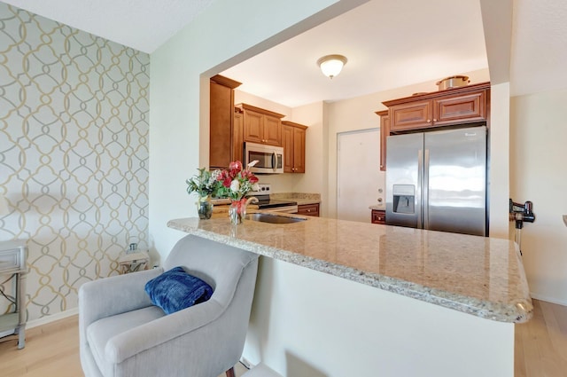 kitchen featuring light stone counters, stainless steel appliances, a peninsula, and light wood finished floors