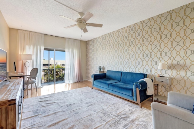 living room featuring wallpapered walls, a ceiling fan, wood finished floors, and a textured ceiling