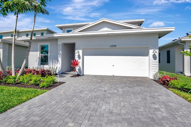 view of front of home with decorative driveway, an attached garage, and stucco siding