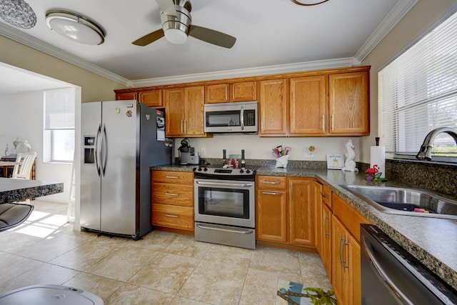 kitchen featuring dark countertops, brown cabinets, stainless steel appliances, crown molding, and a sink