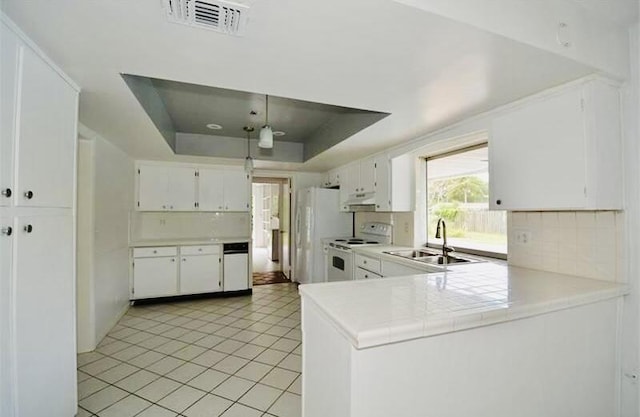 kitchen with a raised ceiling, backsplash, white cabinetry, a sink, and white appliances