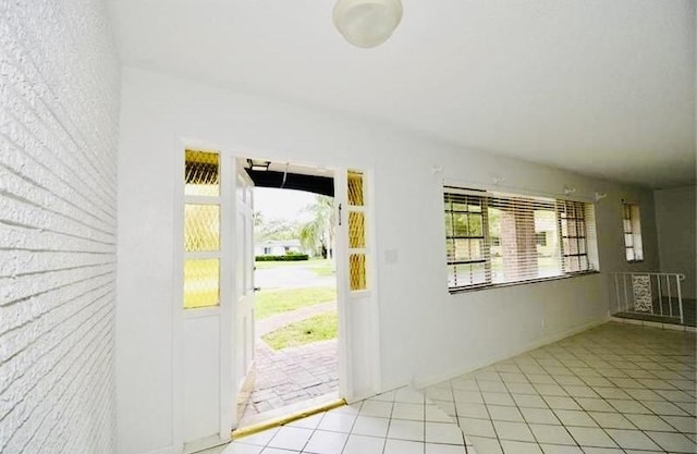 entryway with light tile patterned floors, brick wall, and a wealth of natural light