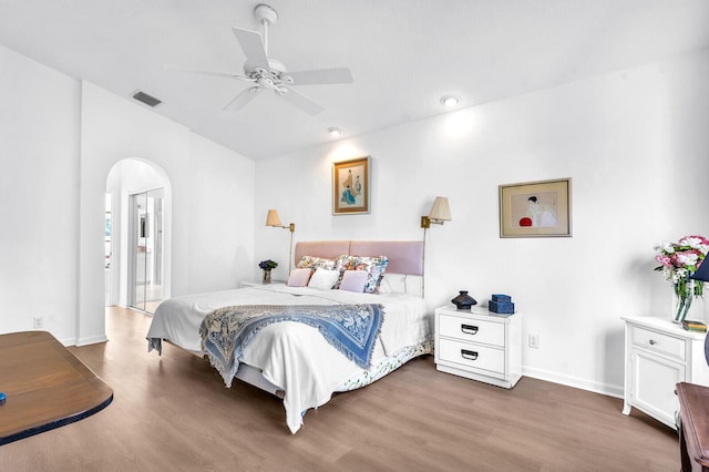 bedroom featuring baseboards, visible vents, arched walkways, ceiling fan, and wood finished floors