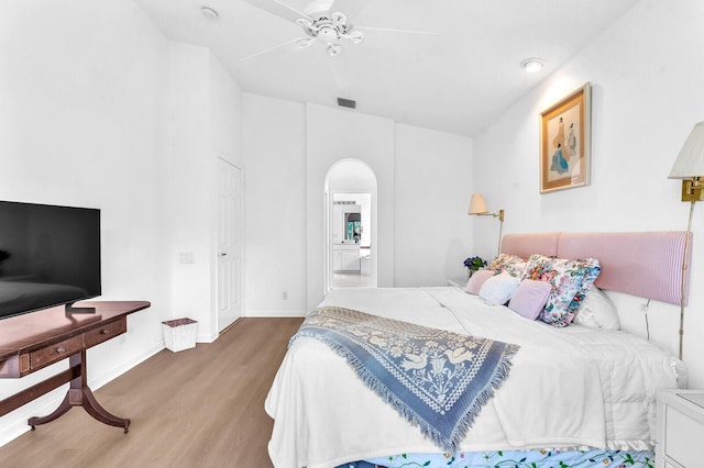 bedroom with arched walkways, ceiling fan, wood finished floors, visible vents, and baseboards