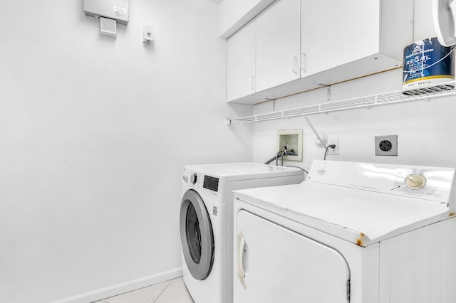 clothes washing area with light tile patterned floors, washing machine and clothes dryer, cabinet space, and baseboards