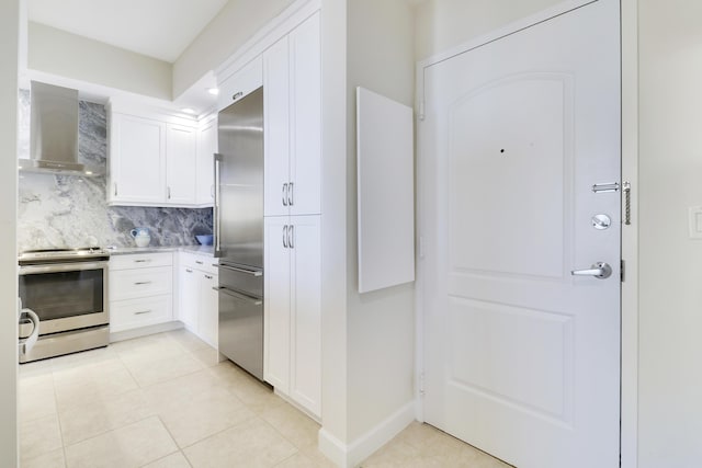 kitchen featuring backsplash, white cabinetry, stainless steel appliances, wall chimney exhaust hood, and light countertops