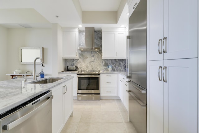 kitchen featuring a sink, backsplash, stainless steel appliances, wall chimney exhaust hood, and light stone countertops