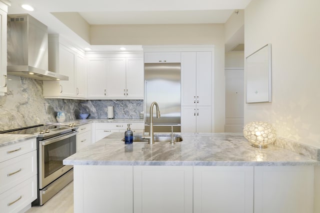 kitchen with light stone counters, backsplash, appliances with stainless steel finishes, and wall chimney range hood