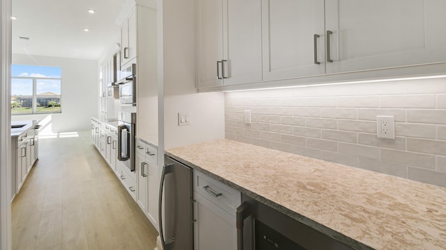 kitchen with beverage cooler, white cabinets, light wood-style floors, light countertops, and backsplash