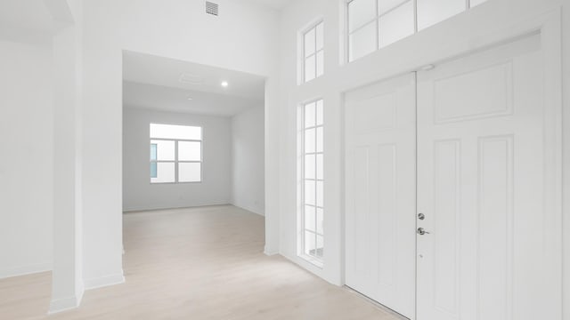 foyer with light wood-type flooring, visible vents, a towering ceiling, and baseboards