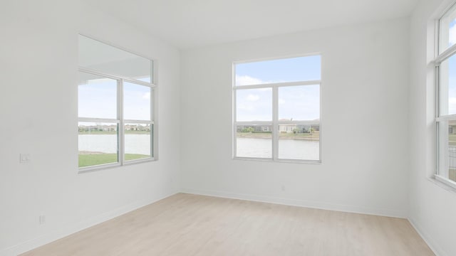 unfurnished room with a healthy amount of sunlight, a water view, and light wood finished floors