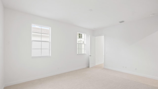 empty room featuring light carpet, visible vents, and baseboards