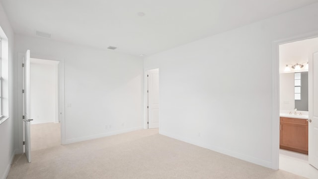 unfurnished bedroom with light carpet, a sink, visible vents, baseboards, and ensuite bath