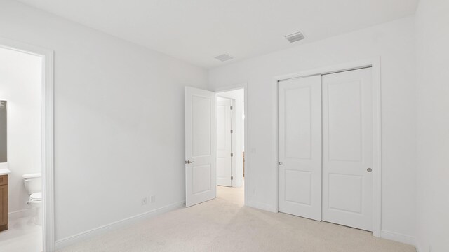 unfurnished bedroom featuring ensuite bathroom, light carpet, visible vents, baseboards, and a closet