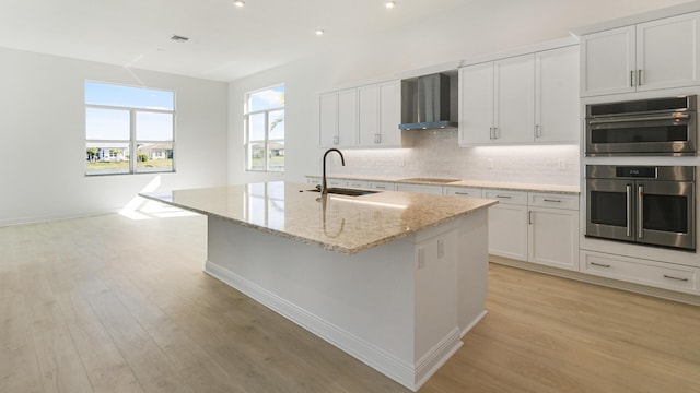 kitchen with tasteful backsplash, black electric cooktop, stainless steel double oven, wall chimney range hood, and a sink