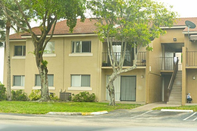 view of property featuring stairway, cooling unit, and uncovered parking