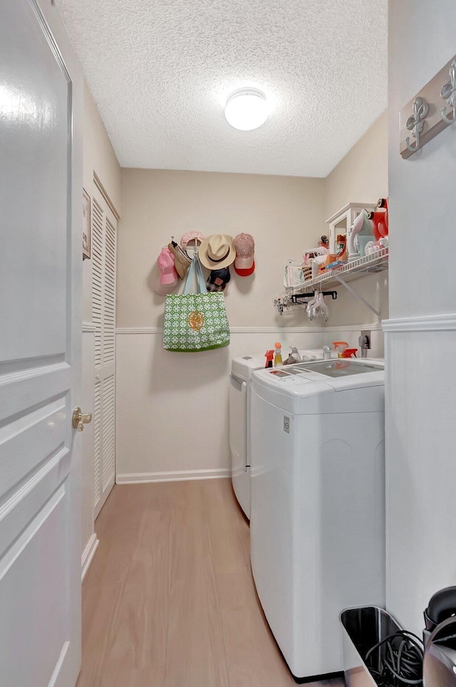 washroom with light wood-style floors, washing machine and dryer, wainscoting, a textured ceiling, and laundry area